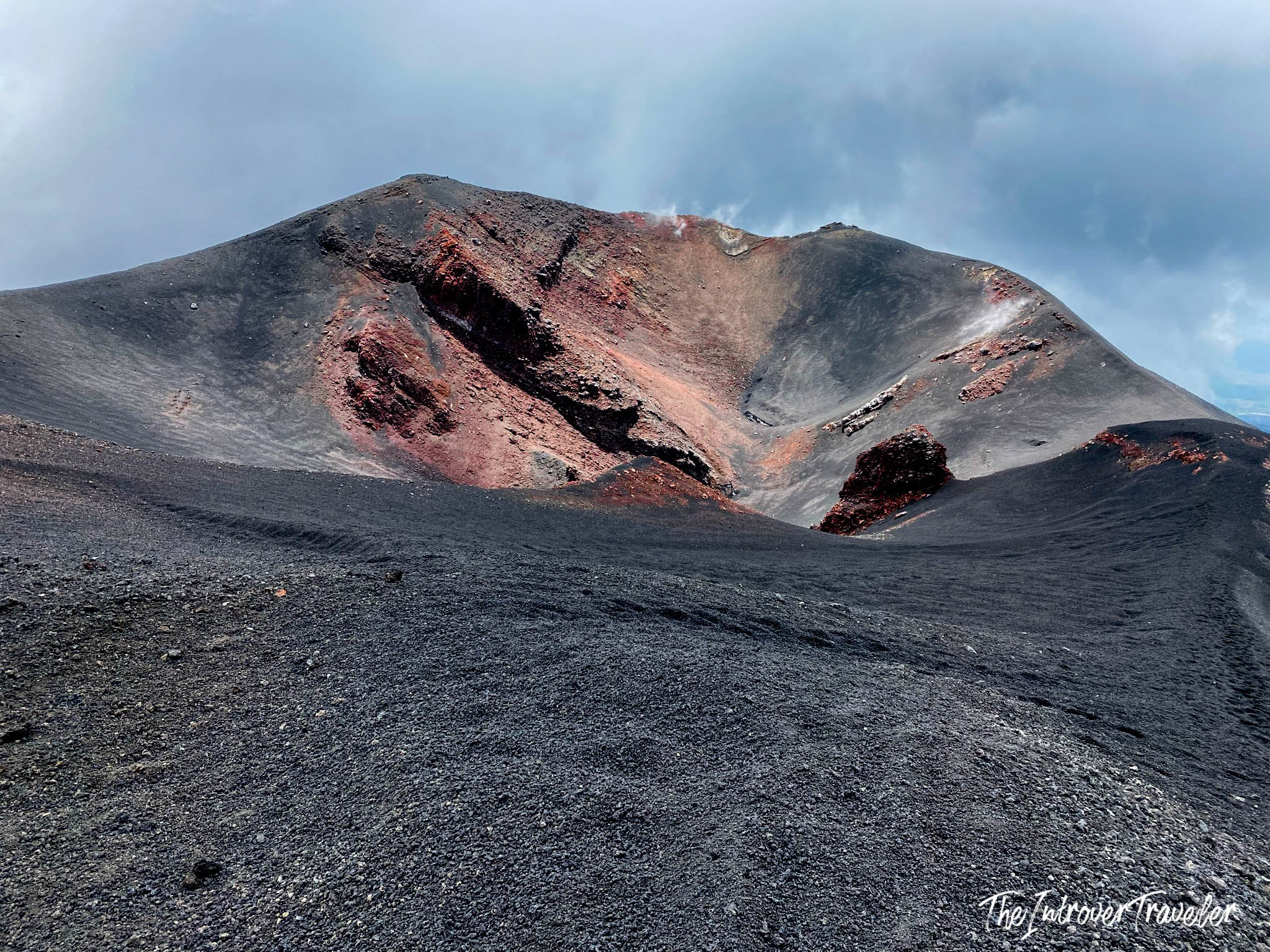 Mount Etna crater rim up close, showing black volcanic ash and red oxidized lava rock formations