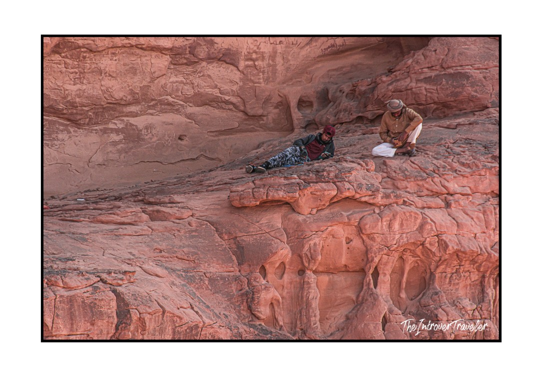 Two Bedouin locals resting on red sandstone rock formations in Wadi Rum desert, Jordan
