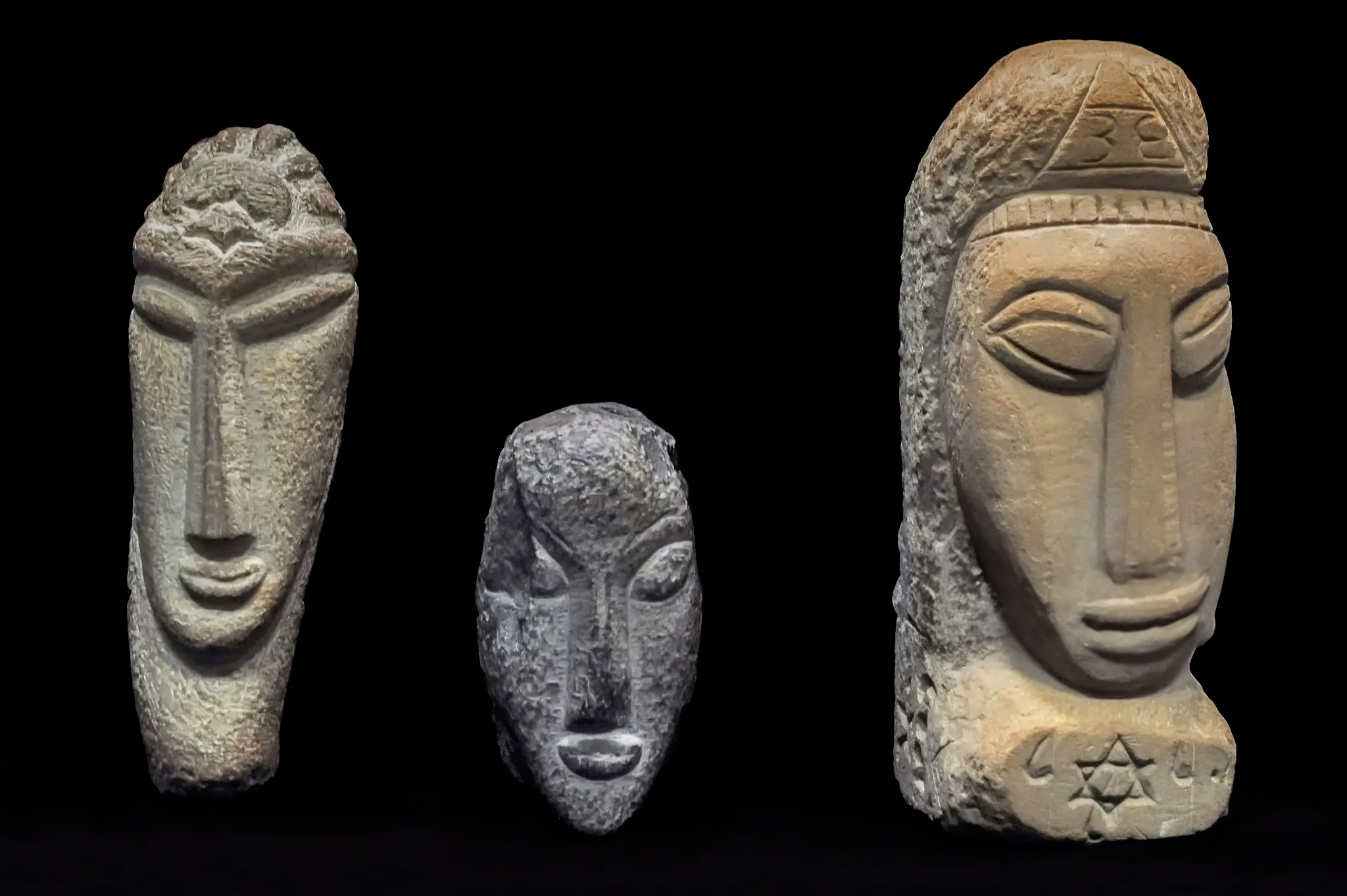 Three carved stone heads from Mont'e Prama, Sardinia, showing elongated stylized faces with symbolic engravings