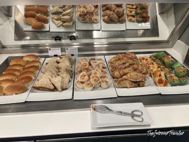 Buffet snack selection at Piranesi Lounge Milan Linate, featuring sandwiches, croissants, and mini muffins