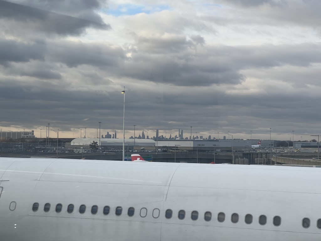 Manhattan skyline silhouette viewed from JFK airport tarmac, with aircraft in the foreground