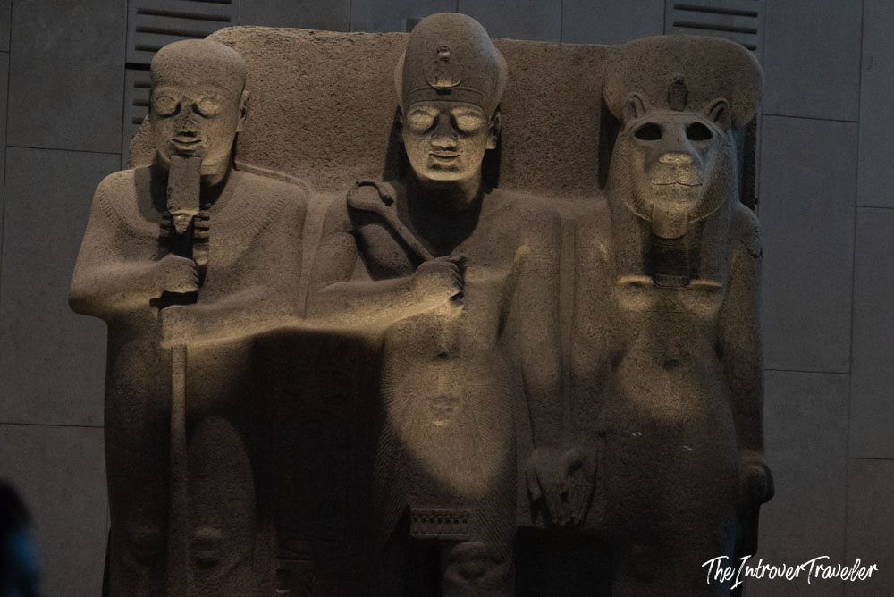 Ancient Egyptian triad sculpture at the Grand Egyptian Museum, featuring a pharaoh flanked by two deities