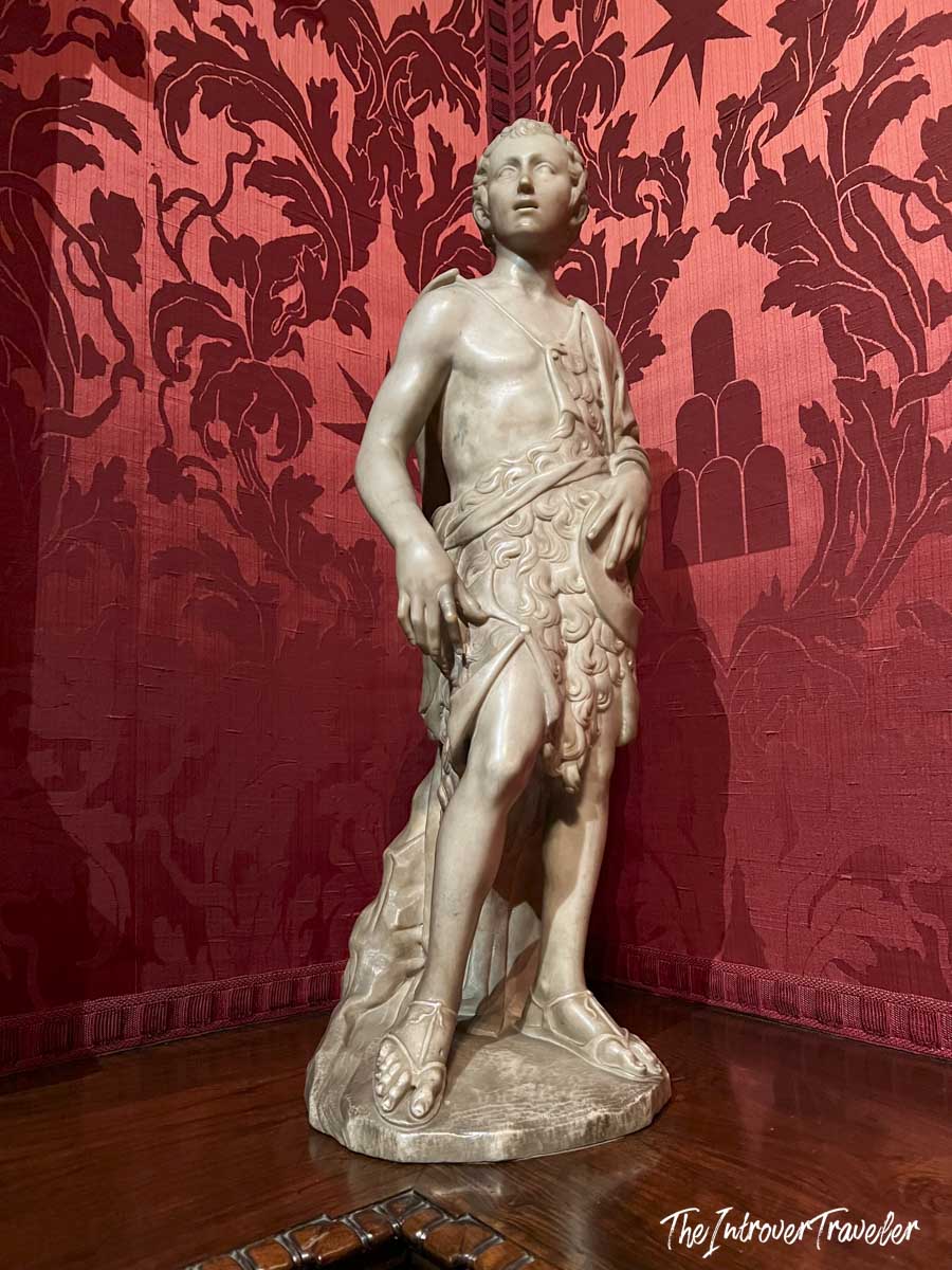 Marble sculpture of a young Saint John the Baptist displayed against red damask walls at the Morgan Library, New York