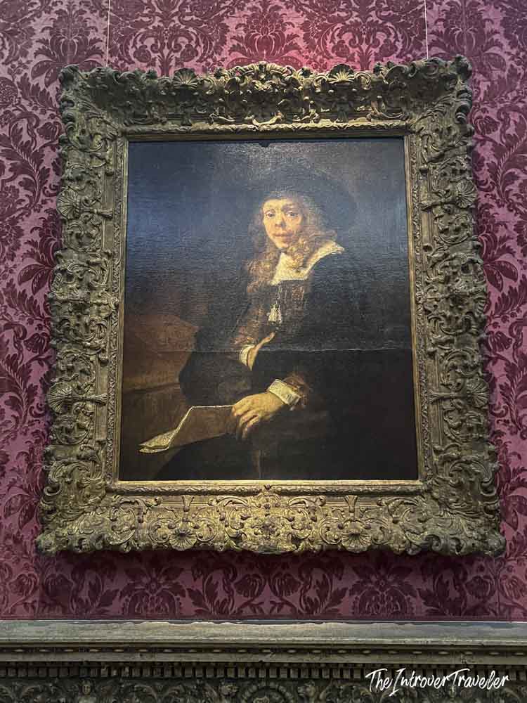 Rembrandt portrait painting in ornate gold frame displayed on red damask wall at the Met