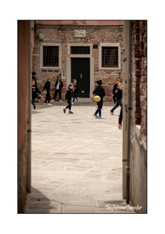 Children playing football in a Venetian campo, framed by a narrow alley doorway