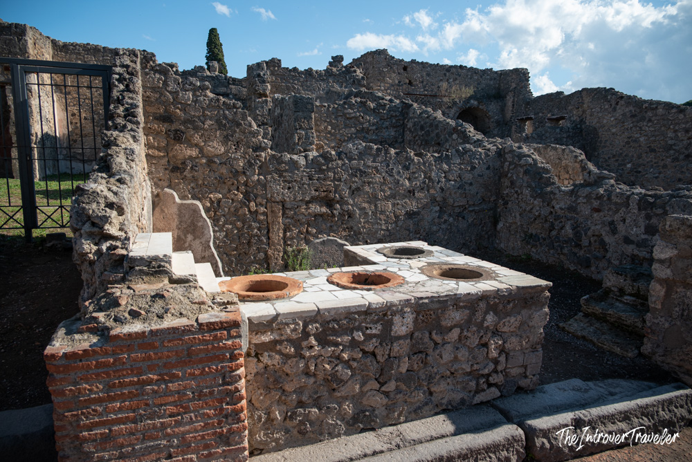 Ancient Roman thermopolium ruins in Pompeii, showing a stone counter with terracotta food vessels