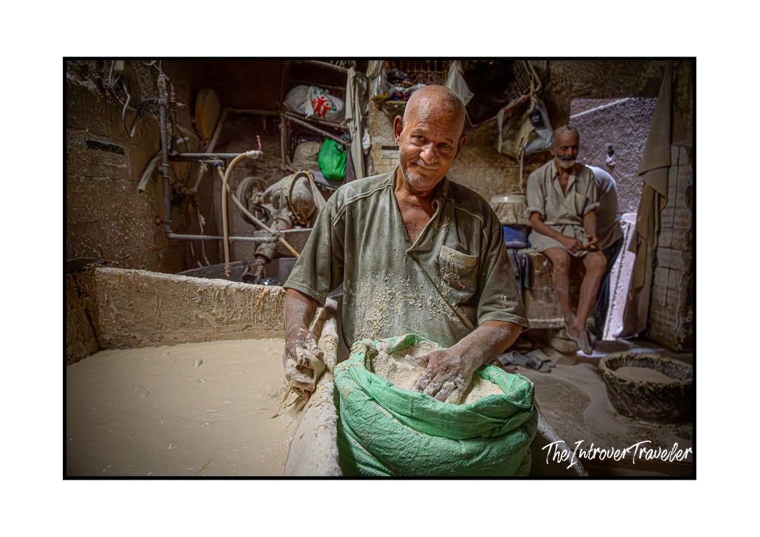 Egyptian baker covered in flour, smiling while kneading dough in a traditional Cairo bakery