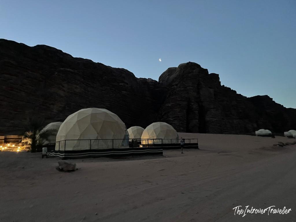 Glowing geodesic dome tents at a Wadi Rum desert camp, Jordan, under a crescent moon at dusk