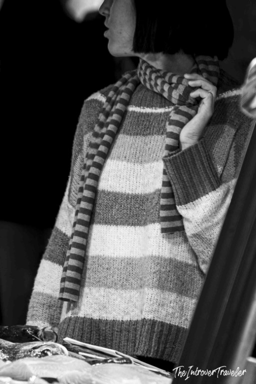 Woman in striped knitwear and scarf browsing stalls at a coastal city fish market