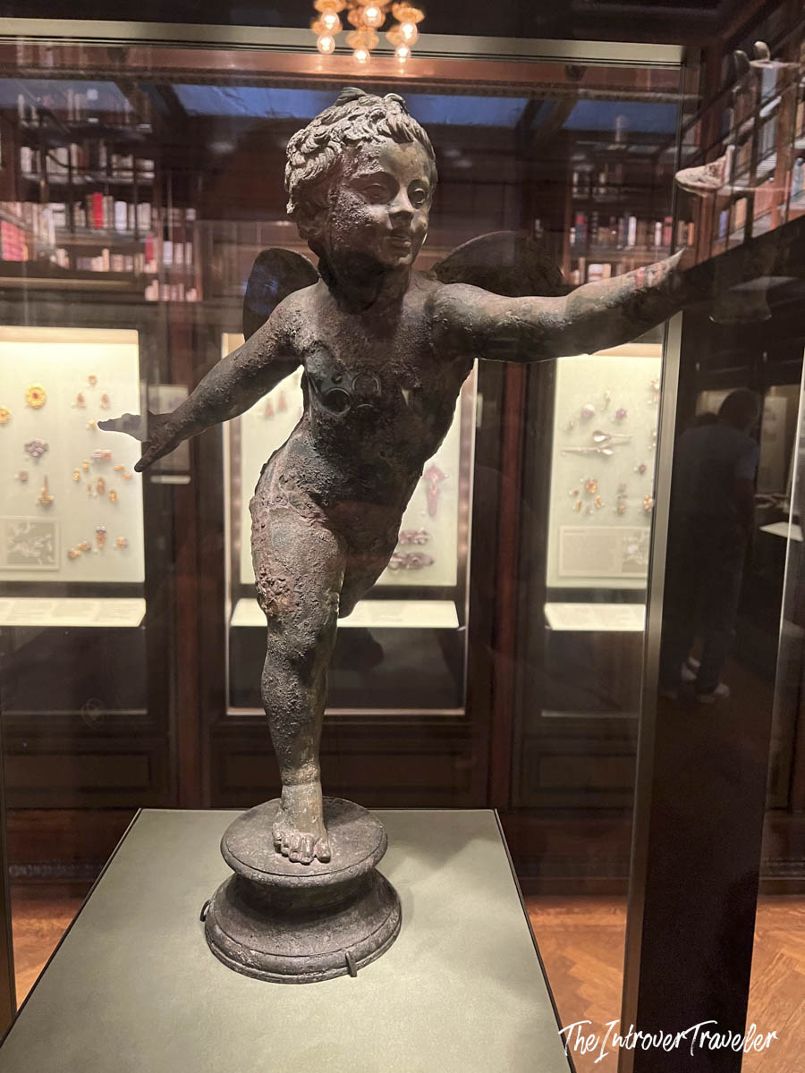 Bronze winged Eros figurine on display in a glass case at the Morgan Library and Museum, New York