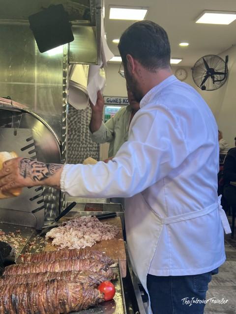Chef preparing kokoreç at Güneş Kokoreç restaurant in Istanbul, slicing grilled offal wraps