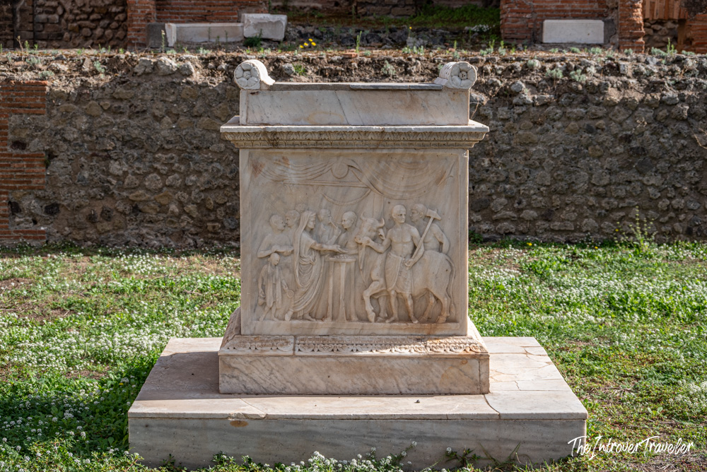 Ancient Roman marble altar with relief carvings of figures, displayed outdoors at Pompeii archaeological site