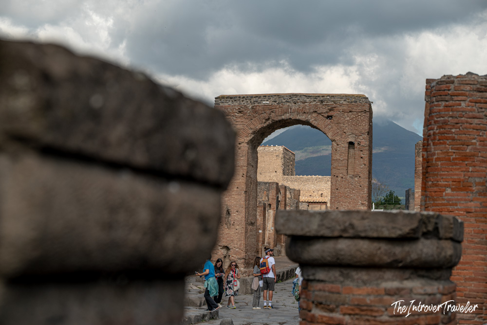 Arch of Caligula in Pompeii with Mount Vesuvius visible through the ruins behind tourists