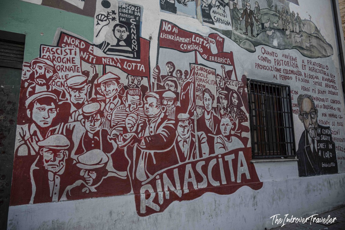 Political mural in Orgosolo, Sardinia, depicting a protest crowd with Rinascita banner and anti-fascist slogans