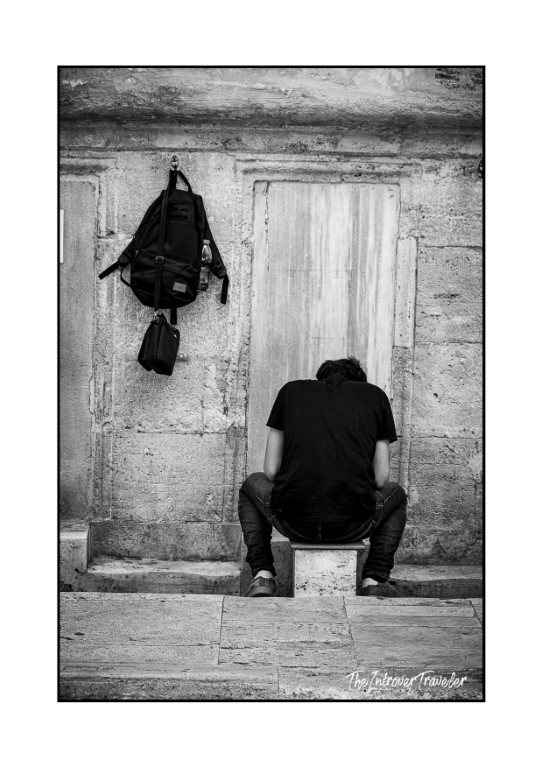 Lone traveler resting on stone steps beside a weathered doorway in Istanbul, backpack hanging nearby