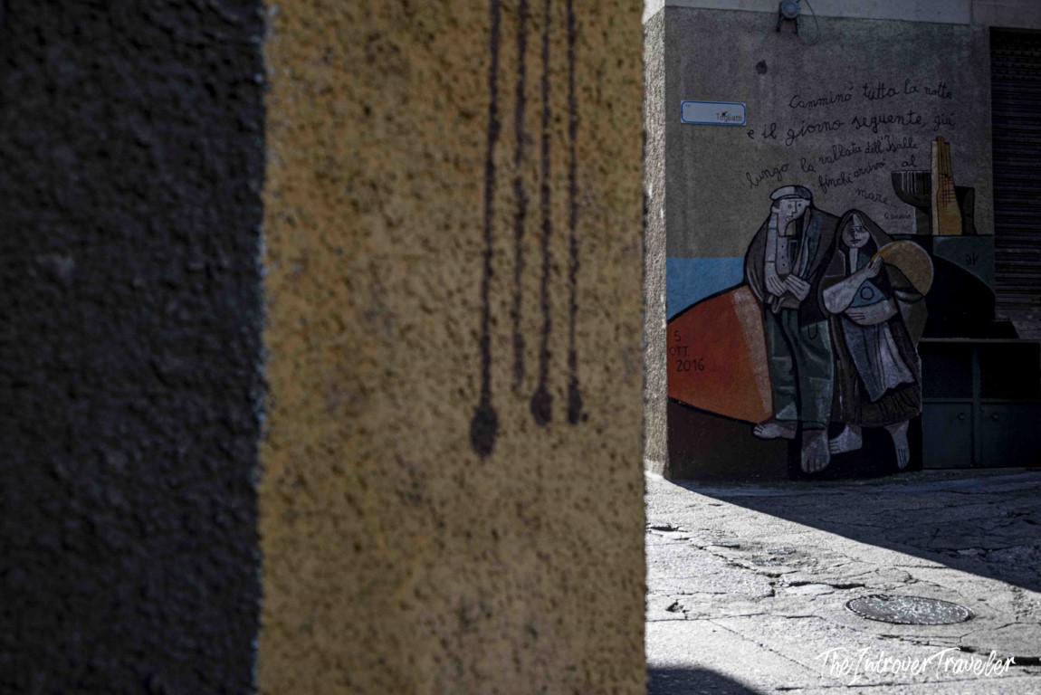 Street mural in Orgosolo, Sardinia, with two figures and an Italian poetic inscription on a village wall