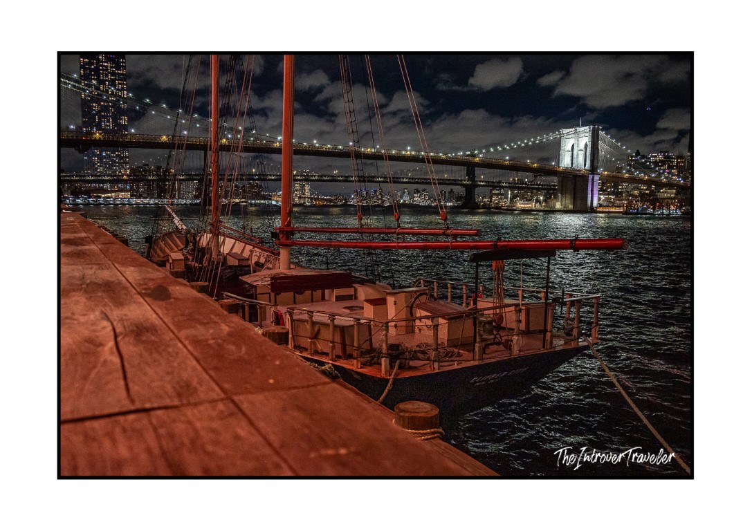 Historic sailing vessel docked on the East River waterfront with Brooklyn Bridge lit up at night