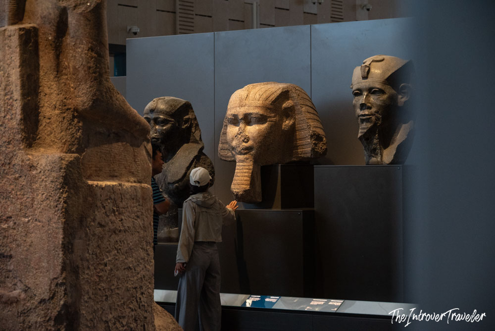 Visitor examining ancient pharaoh head sculptures in the Grand Egyptian Museum, Cairo