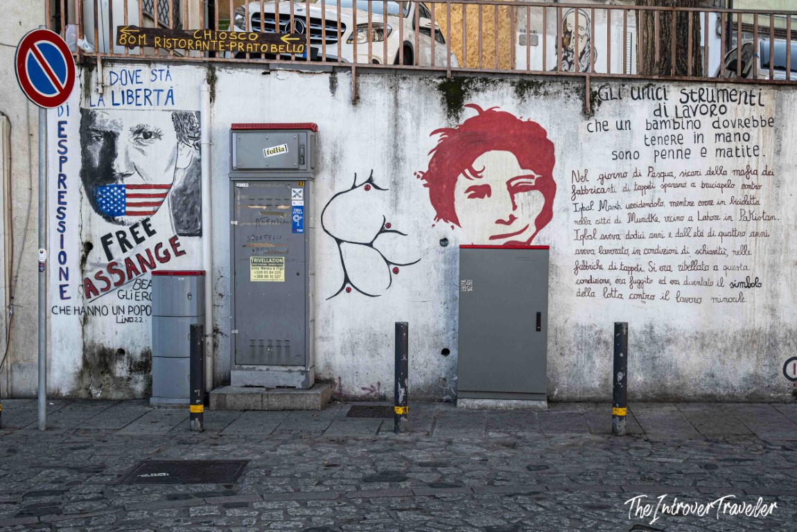 Orgosolo murals featuring Free Assange portrait and Iqbal Masih tribute with Italian text on cobblestone street