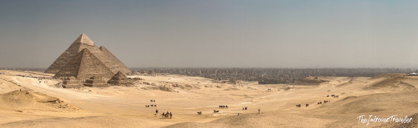 Panoramic view of the Pyramids of Khafre and Khufu at Giza, with camels and Cairo skyline beyond