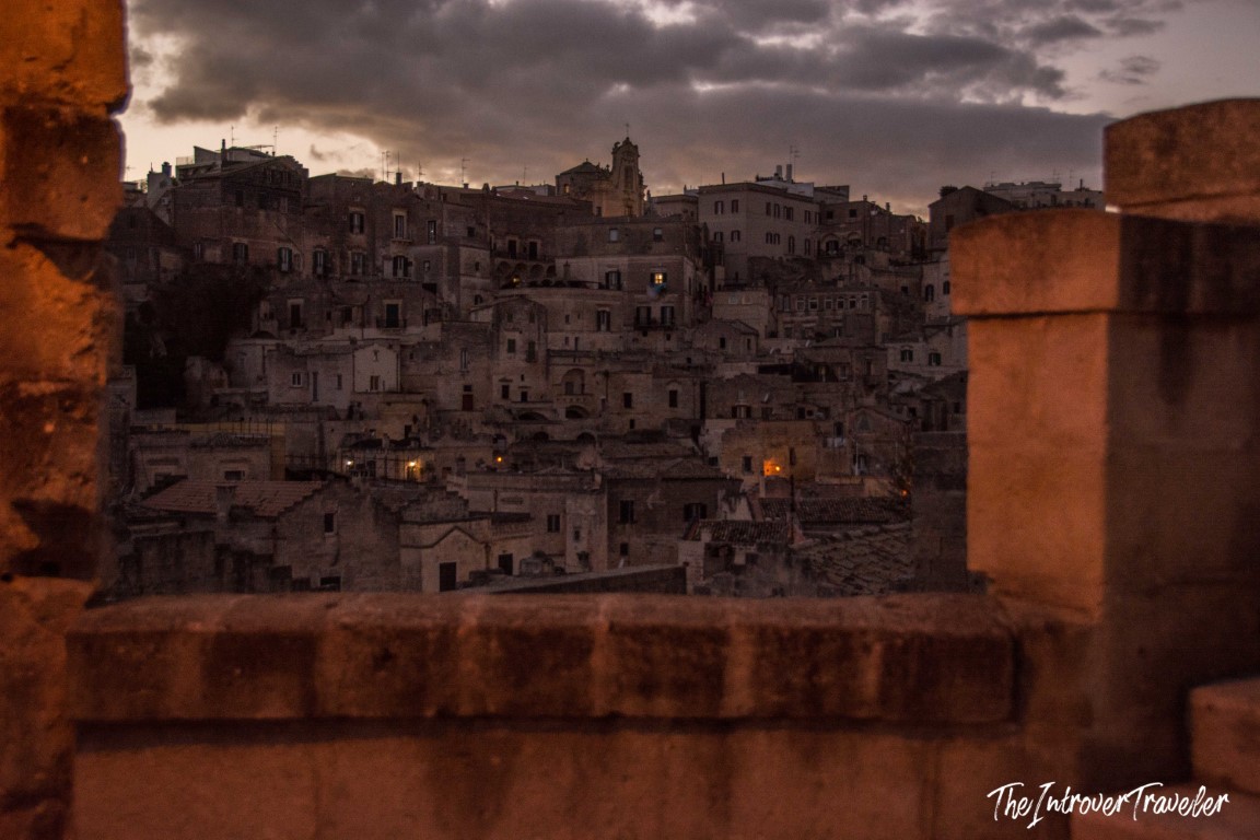 Matera Sassi cave dwellings at dusk, framed by ancient stone walls under a dramatic cloudy sky