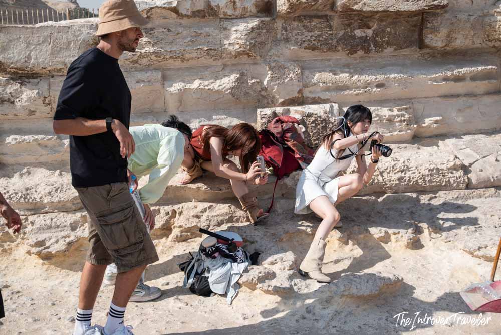Tourists crouching and photographing at the base of the Pyramids of Giza limestone blocks