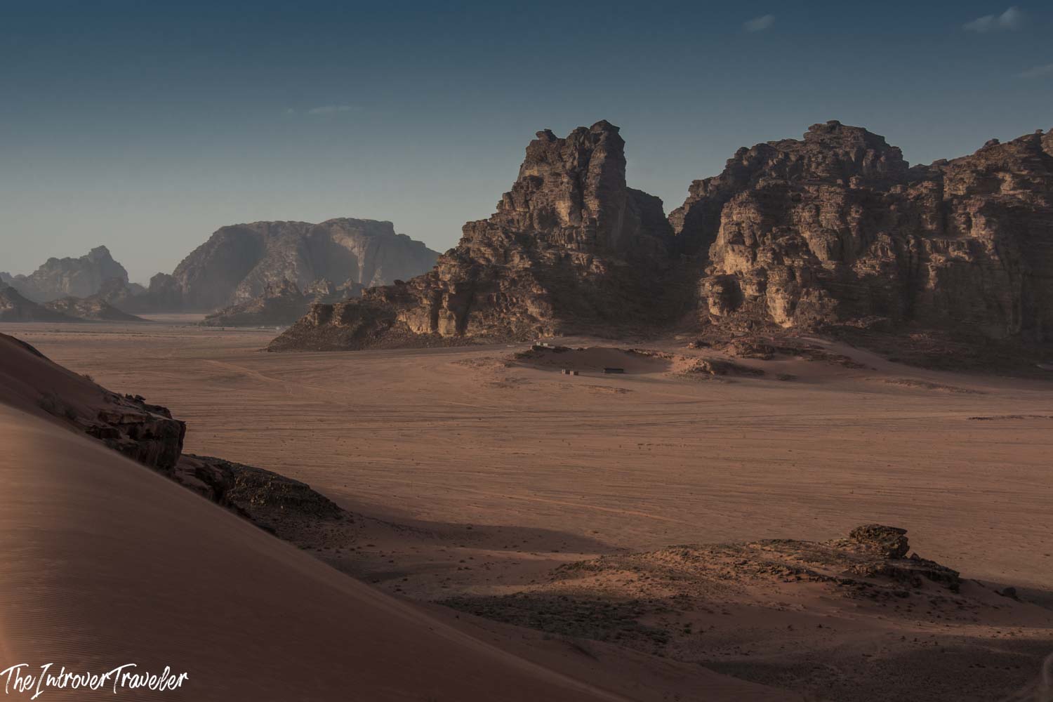 Vast red sand plains and jagged sandstone cliffs of Wadi Rum desert, Jordan, under a clear blue sky