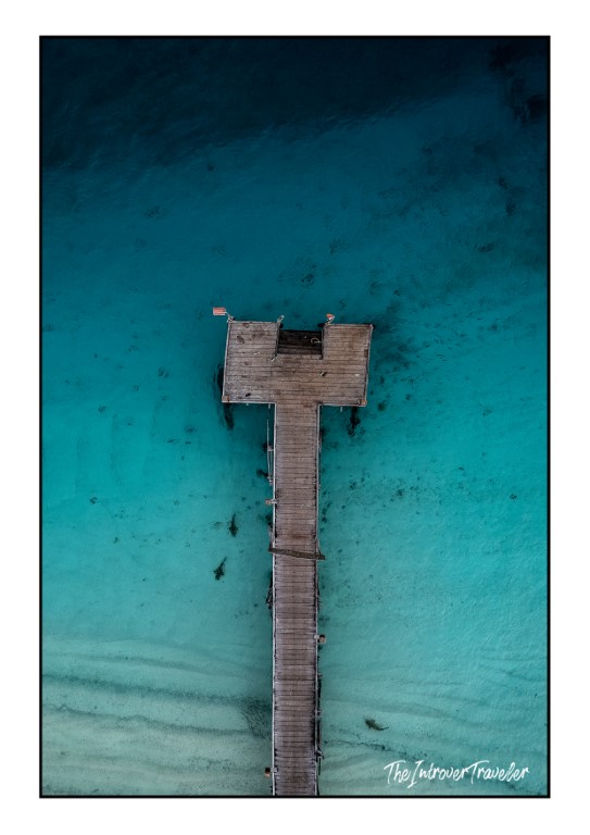 Aerial drone view of a wooden dive jetty over crystal-clear turquoise waters in Raja Ampat, Indonesia