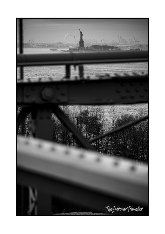 Statue of Liberty framed through steel bridge girders, black and white New York street photography