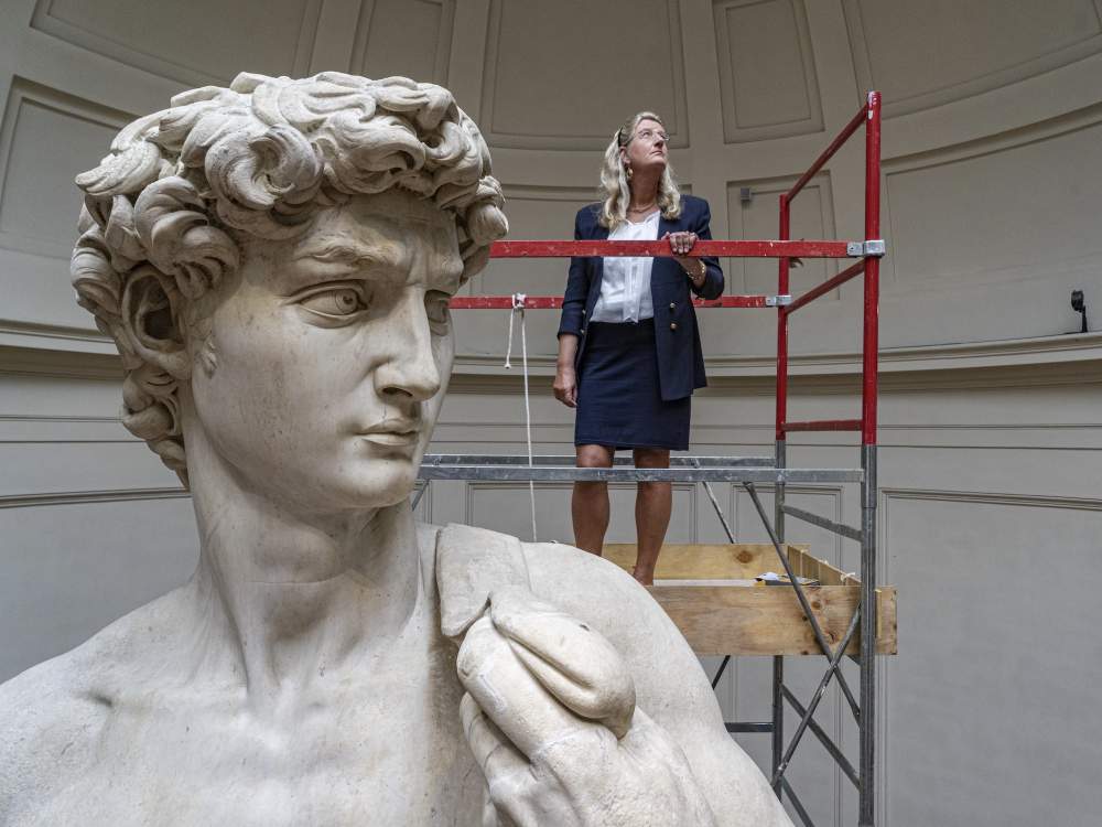 Conservator on scaffolding examining Michelangelo's David up close at the Galleria dell'Accademia, Florence