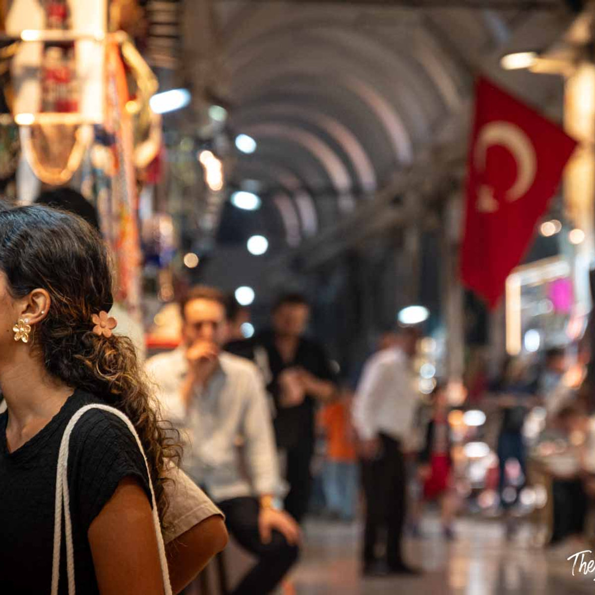 Woman browsing the Grand Bazaar in Istanbul, with arched corridors and a Turkish flag in the background