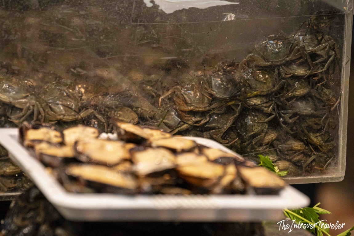 Live crabs piled in a tank beside fresh shellfish at a bustling coastal city fish market