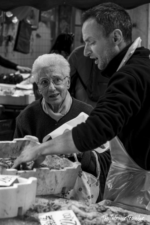 Elderly woman and fishmonger talking over fresh catch at a lively coastal city fish market
