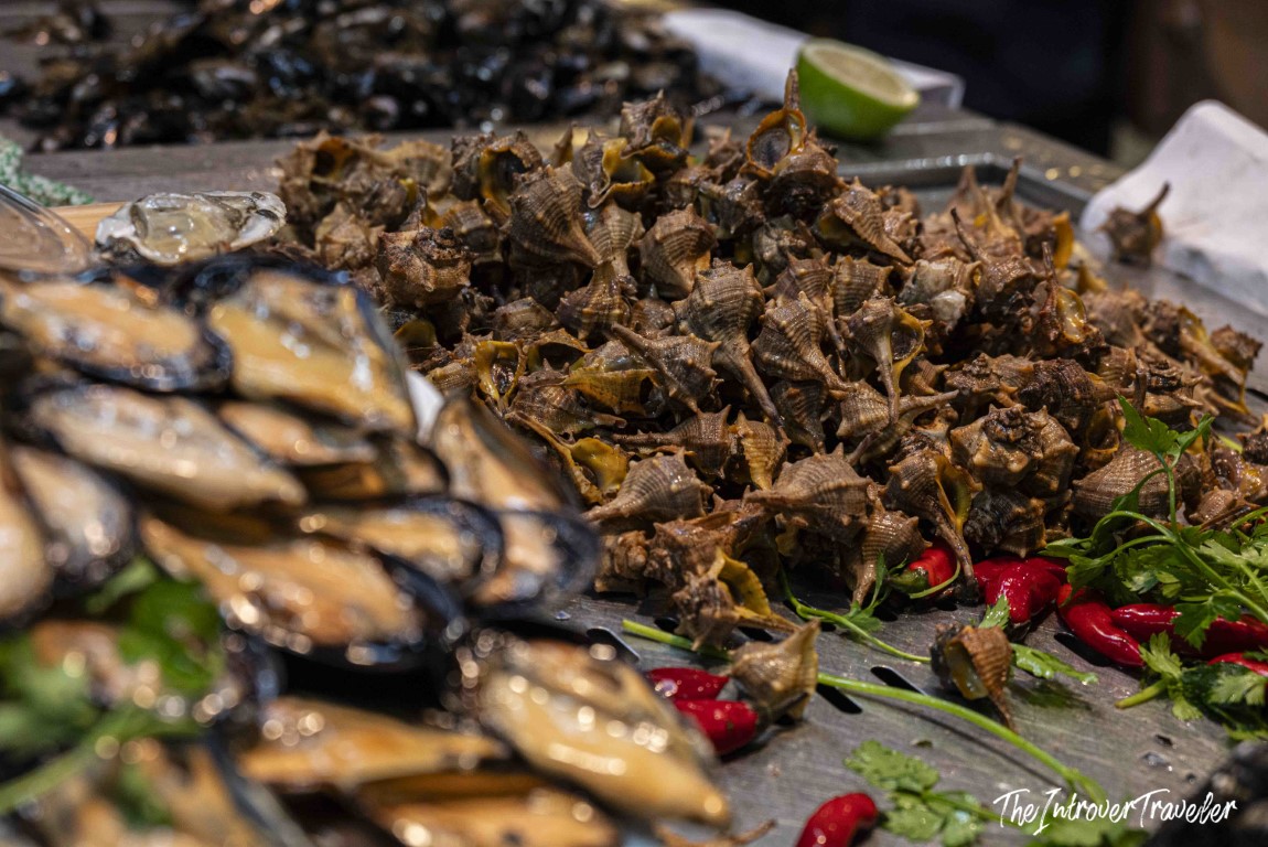 Fresh murex sea snails and mussels displayed at a coastal fish market, garnished with chili and herbs