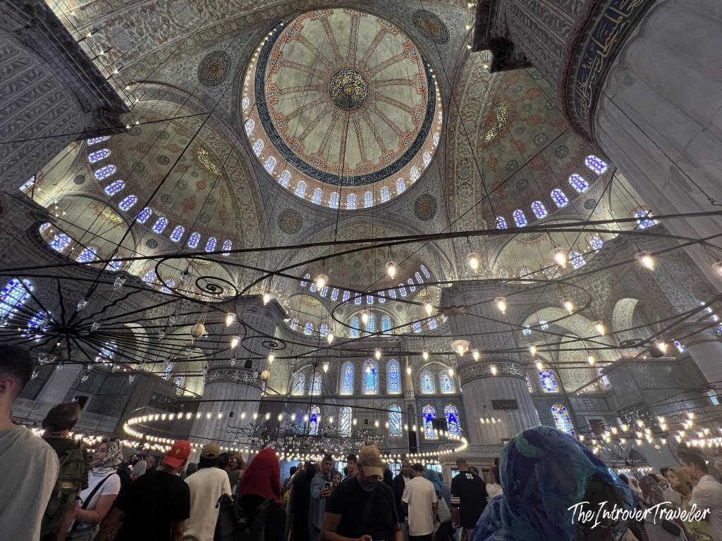 Interior of the Blue Mosque in Istanbul, showing its grand dome, stained glass windows, and hanging chandeliers