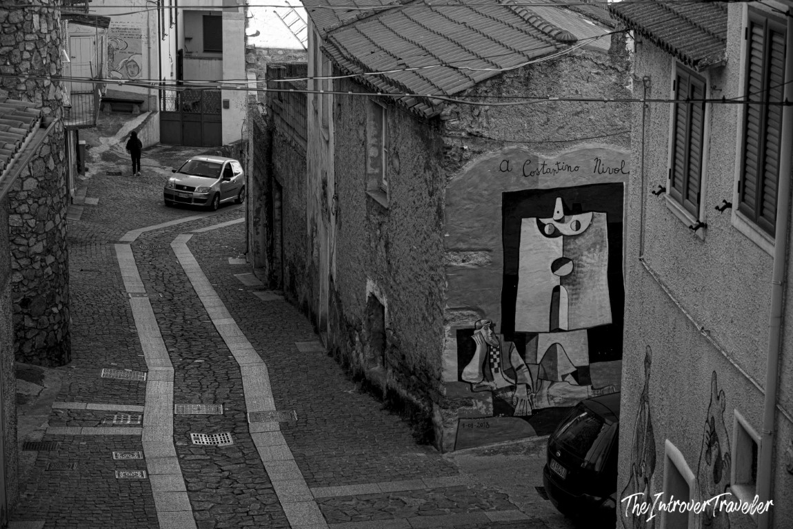 Cubist-style mural dedicated to Costantino Nivola on a cobblestone street in Orgosolo, Sardinia