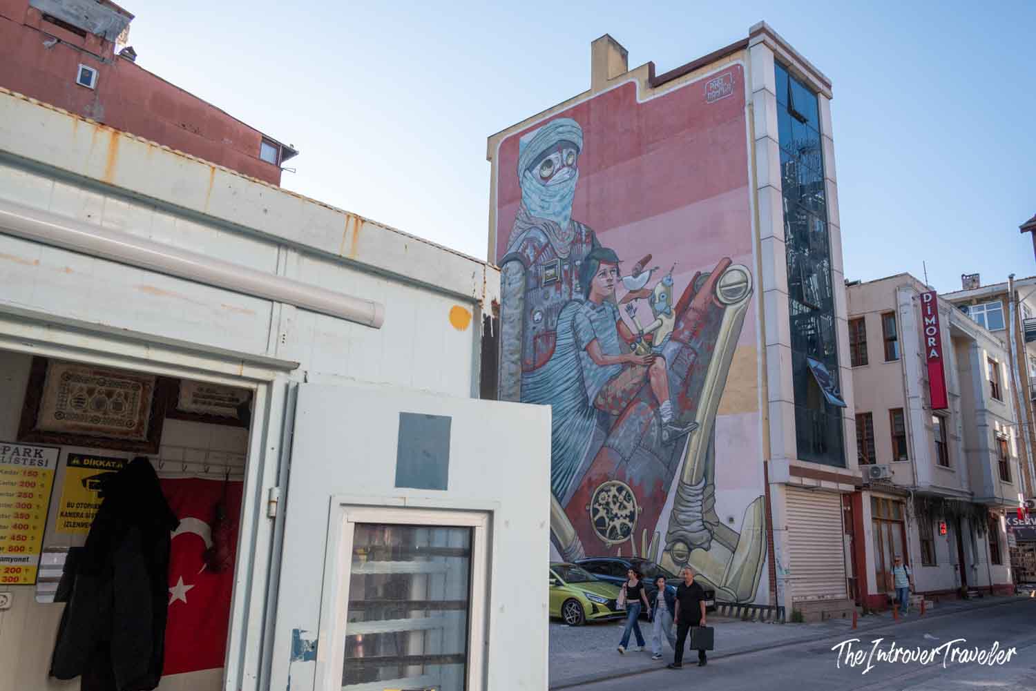 Large street art mural on a building facade in Kadıköy, Istanbul, depicting a cloaked figure and child with mechanical elements