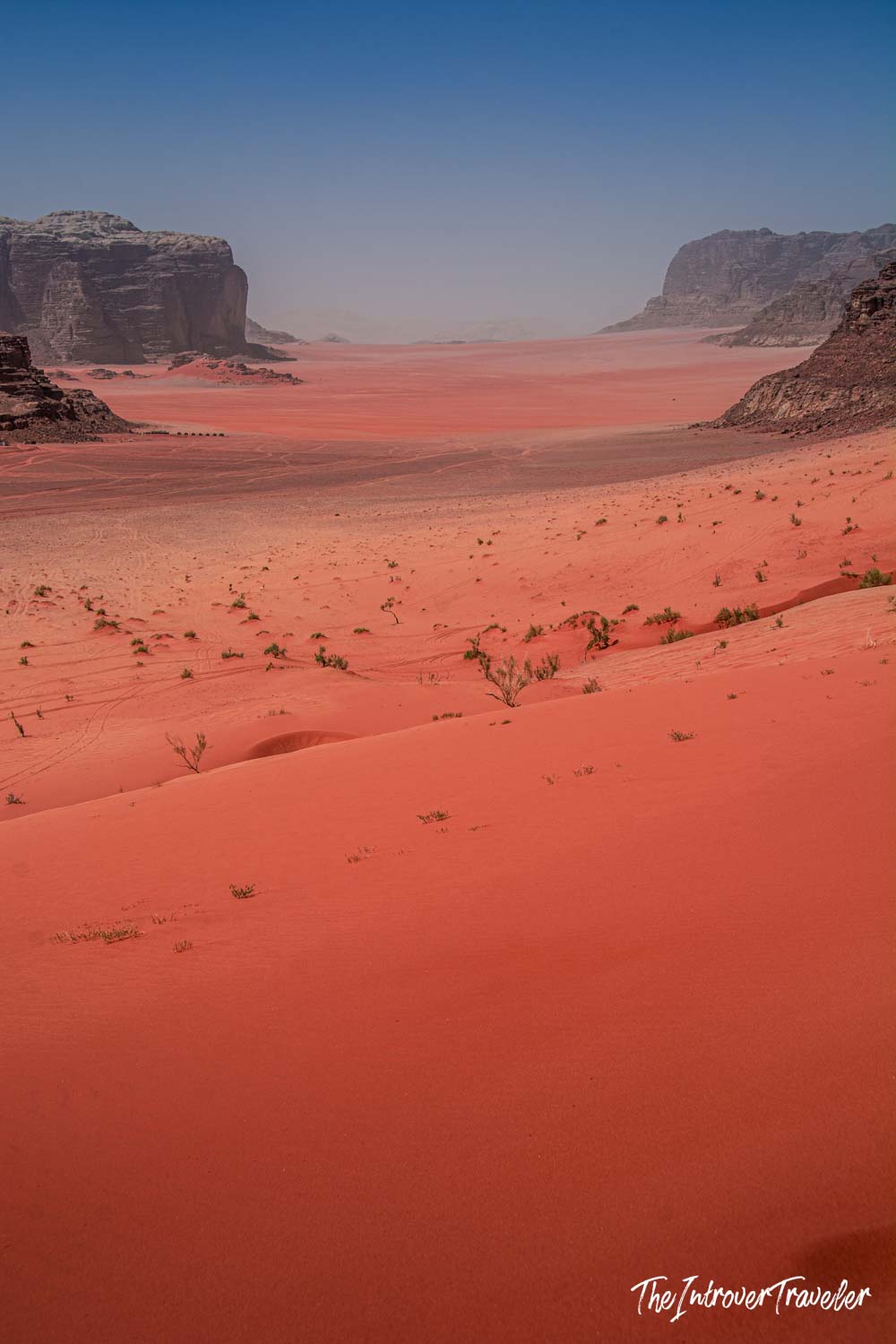 Vast red sand dunes and sandstone cliffs of Wadi Rum desert, Jordan, under a hazy blue sky