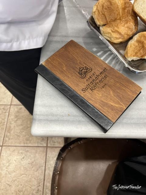 Wooden menu cover of Tarihi Sultanahmet Köftecisi restaurant, Istanbul, beside fresh bread rolls