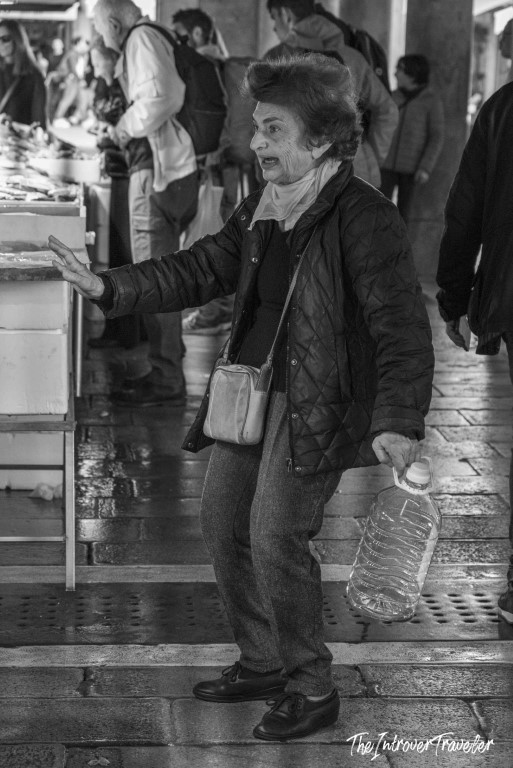 Animated elderly woman carrying a water bottle and gesturing at a busy coastal fish market