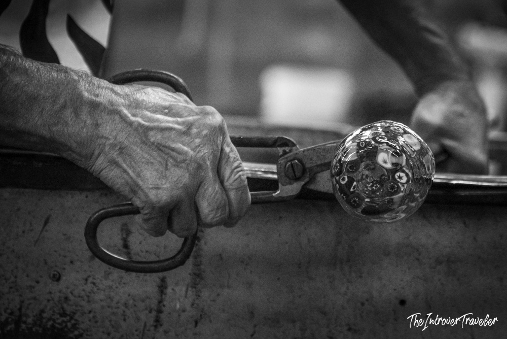 Murano glassmaker shaping a millefiori glass sphere with metal tongs on the island of Murano, Venice