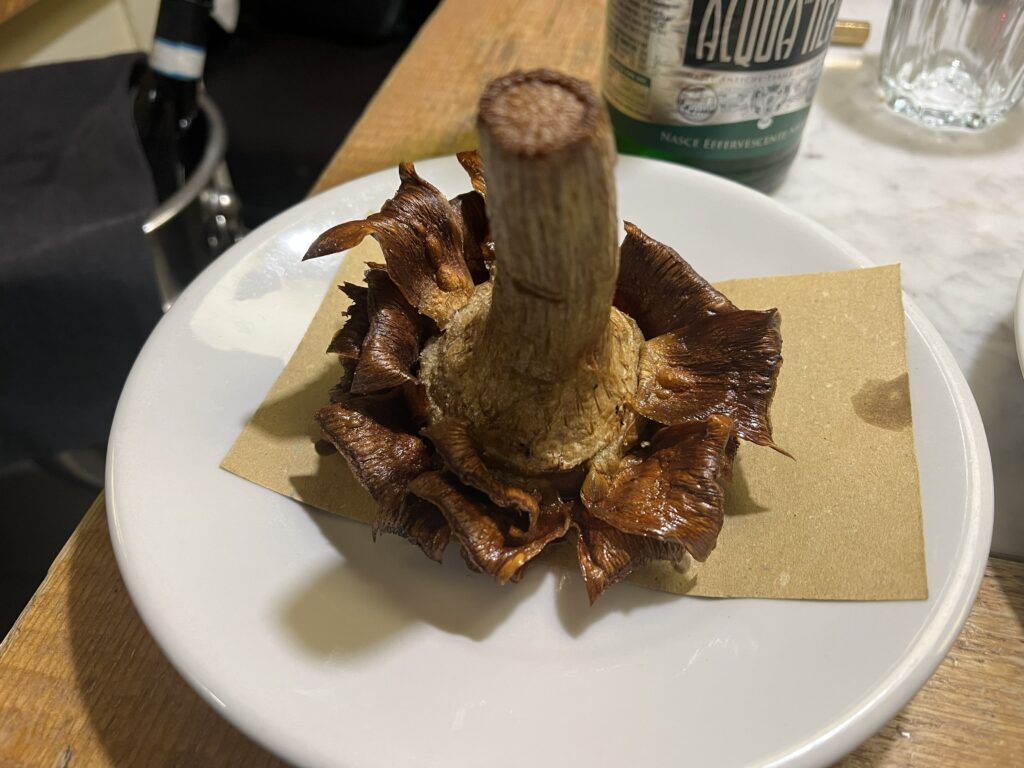 Whole roasted porcini mushroom served upright on parchment at Osteria La Quercia, Rome