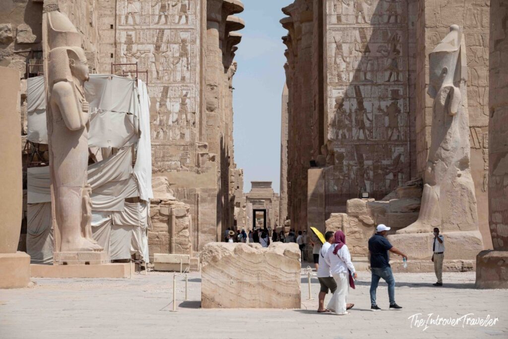 Tourists walking between colossal Ramesses II statues at the entrance to Karnak Temple Complex, Luxor