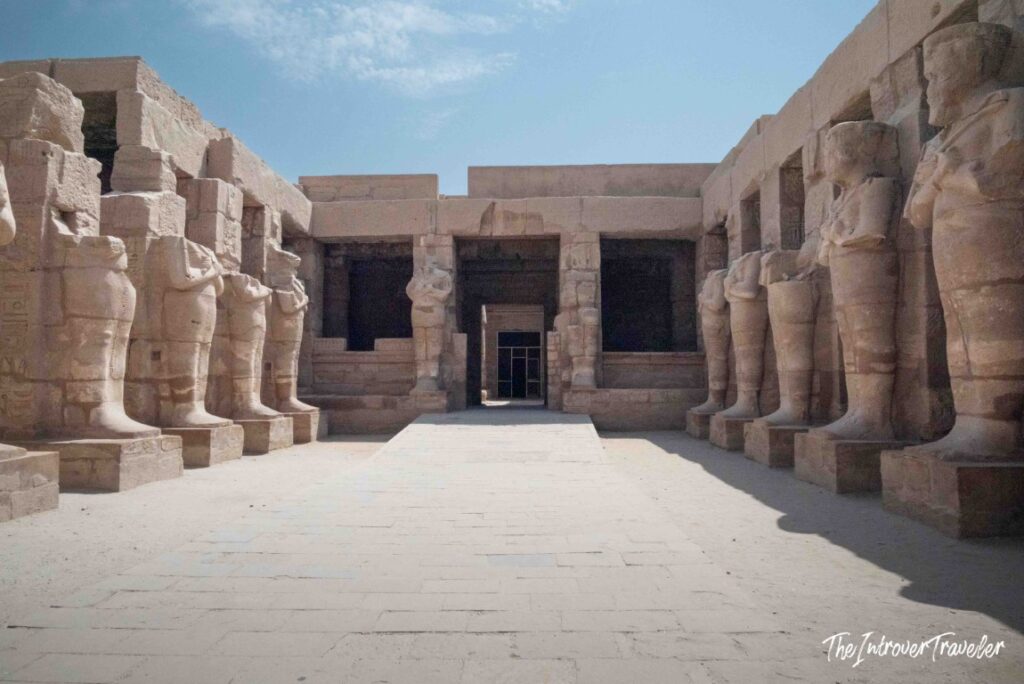 Karnak Temple courtyard lined with ancient Egyptian pharaoh statues leading to a sanctuary entrance, Luxor