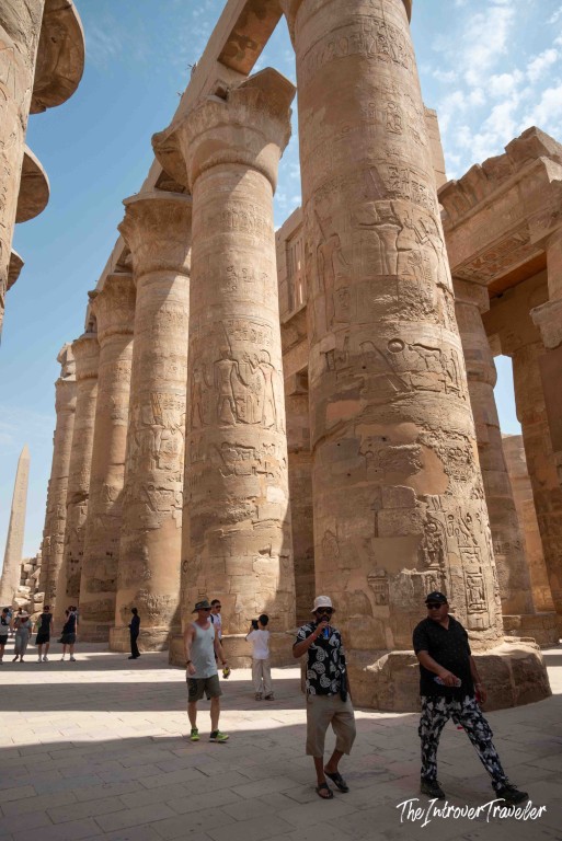 Tourists dwarfed by massive hieroglyph-covered columns in the Hypostyle Hall, Karnak Temple, Luxor