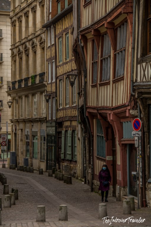 Lone traveler walking past medieval half-timbered buildings on a cobblestone street in Rouen, Normandy