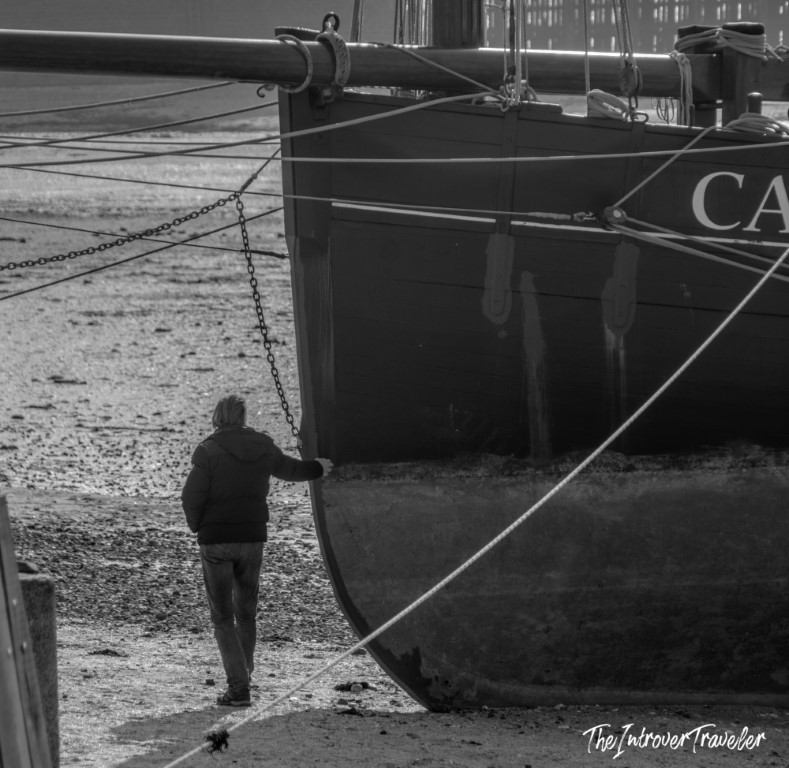 Man standing beside a tall sailing vessel moored on the tidal flats of Cancale harbour at low tide