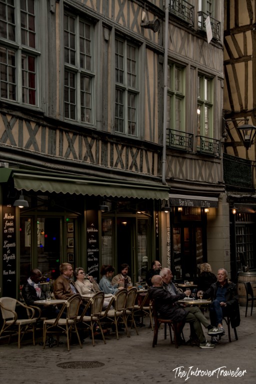 Locals relaxing at a pavement cafe beneath medieval half-timbered facades in Rouen, Normandy