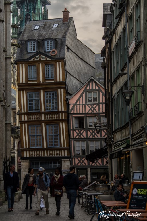 Pedestrians walking past colorful half-timbered medieval buildings in Rouen, Normandy