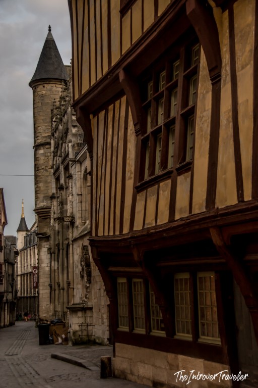 Half-timbered medieval building on a narrow street in Rouen, Normandy, with a Gothic church tower behind